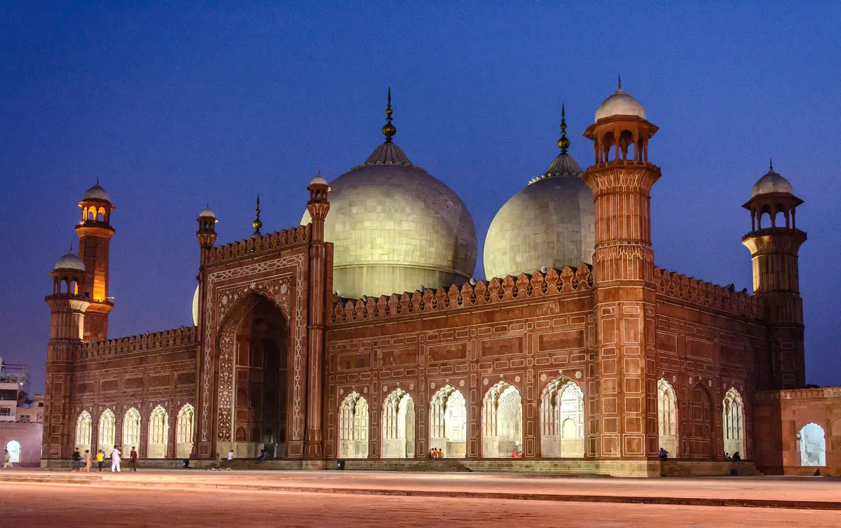 The domes and minarets of the Badshahi Mosque in Lahore, lit against a deep blue evening sky